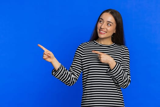Happy Caucasian beautiful woman showing thumbs up and pointing left empty place advertising area for commercial text copy space for goods promotion advertisement. Girl isolated on blue background