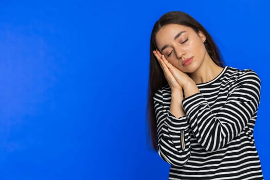 Tired exhausted young Caucasian woman yawning sleepy inattentive feeling somnolent lazy bored gaping suffering from lack of sleep insomnia. Brunette girl isolated on blue studio background. Copy-space