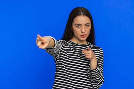Get out of here. You are fired. Caucasian woman pointing finger away asking to leave her alone, strict boss firing conflict quarrel. Strict girl isolated on blue studio background indoors. Copy-space