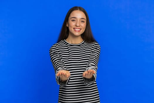 Free gifts and presents for you. Caucasian young woman in striped blouse opening hands, excitement, preparing surprise, sharing love emotions, congratulating, charity donation. Girl on blue background