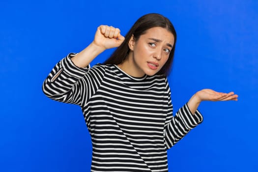 Knock-knock who is there. Confused excited Caucasian woman knocking door gesture asking who is at home feeling embarrassed, no idea being clueless and uncertain. Young girl isolated on blue background