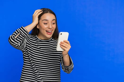 Happy excited young woman girl use smartphone typing browsing shouting say wow yes found out great big win good news lottery goal achievement celebrating success, winning play game on blue. Copy-space
