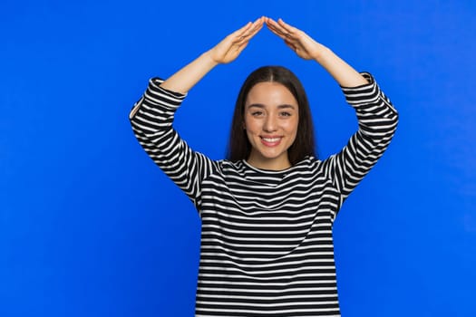 House roof about head. Young woman playing childish catching up game feeling in safe making roof above head with hands, insurance, security service. Girl isolated on blue studio background. Copy-space
