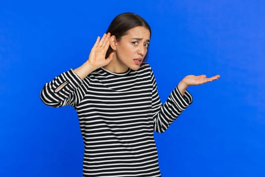 I cant hear you. What. Young Caucasian woman trying hear you looking confused and frowning keeping arm near ear for louder voice asking to repeat to hear information deafness. Girl on blue background