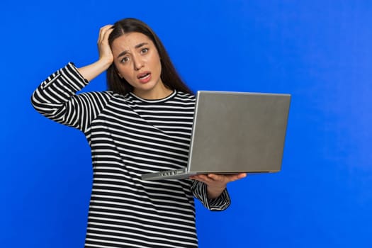 Displeased woman in striped blouse use laptop notebook typing browsing working, loses becoming surprised sudden lottery results bad news fortune loss game fail computer virus. Girl on blue background.