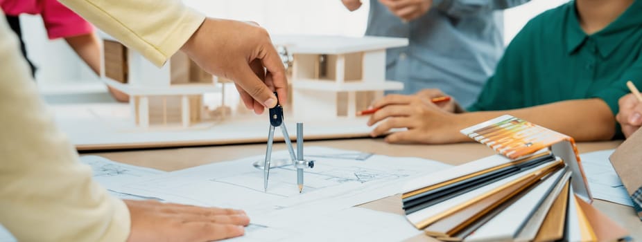 Professional architect team select sustainable house materials while skilled engineer using divider measure blueprint with house model and color palette placed on meeting table. Closeup. Variegated.