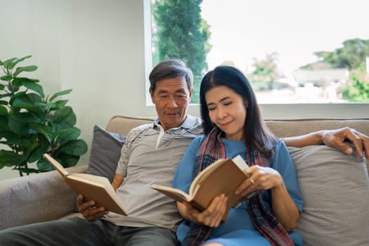 Retired elderly couple sits on couch in their home reading relaxing book. Senior Activity Concept.