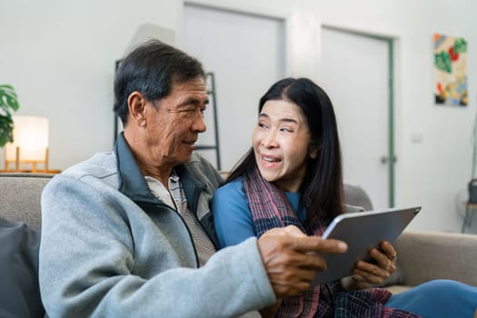 Retired elderly couple sits on couch using tablet together and relax in their home. Senior Activity Concept.