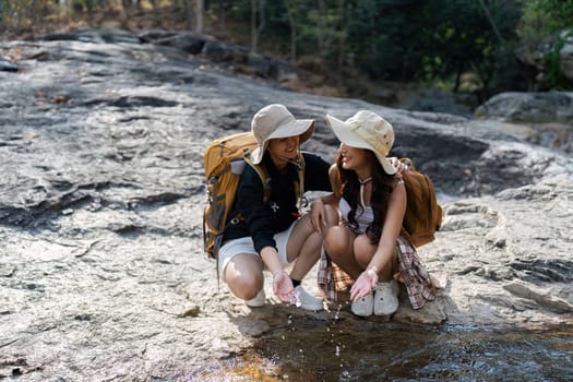 Happy LGBT Lesbian couple Travelers Hiking with Backpacks in waterfall Trail. LGBT Lesbian Couple Hikers with backpacks walks in mountains in vacation.
