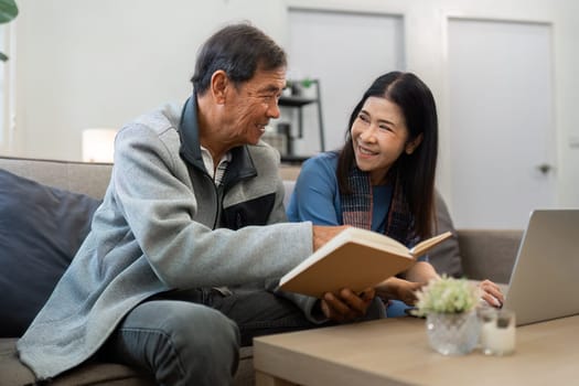 Retired elderly couple sits on couch in their home reading relaxing book. Senior Activity Concept.