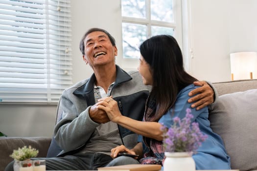 Older couples sit and chat and head over each other relaxed and happy on sofa at home on weekday in comfortable.