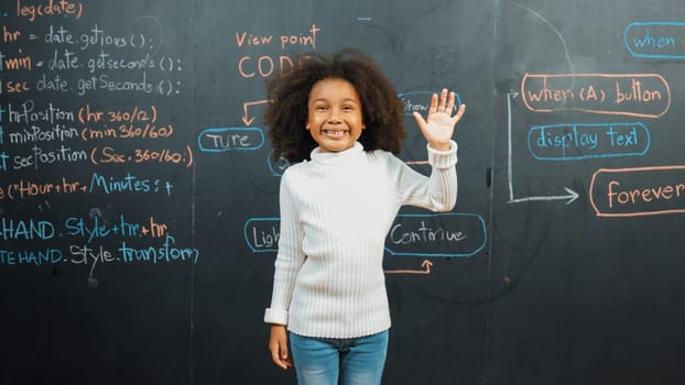 Happy african girl writing blackboard and turnaround to waving at camera while standing at board with engineering prompt or coding, programing system written in STEM technology classroom. Erudition.