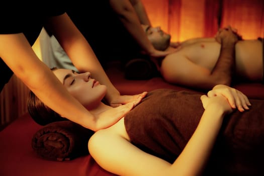 Caucasian couple customer enjoying relaxing anti-stress spa massage and pampering with beauty skin recreation leisure in warm candle lighting ambient salon spa at luxury resort or hotel. Quiescent