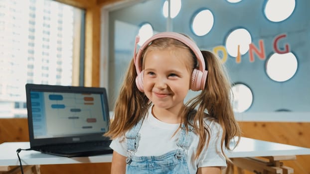 Little pretty caucasian girl smiling to camera while laughing in funny mood. Young child wearing headphone and casual dress standing while looking at camera with satisfy, happy, joyful. Erudition.