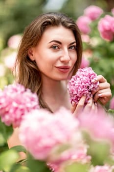 Hydrangeas Happy woman in pink dress amid hydrangeas. Large pink hydrangea caps surround woman. Sunny outdoor setting. Showcasing happy woman amid hydrangea bloom