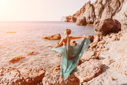 Woman green dress sea. Woman in a long mint dress posing on a beach with rocks on sunny day. Girl on the nature on blue sky background