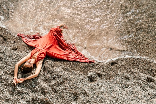 Woman red dress sea. Female dancer in a long red dress posing on a beach with rocks on sunny day.