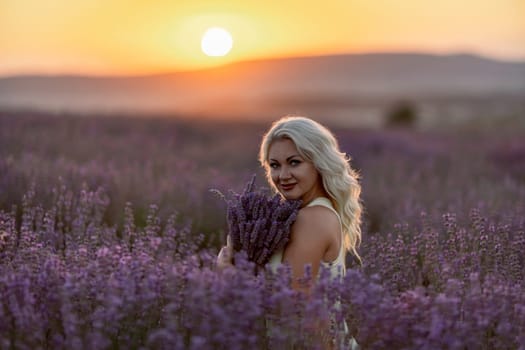 Blonde woman poses in lavender field at sunset. Happy woman in white dress holds lavender bouquet. Aromatherapy concept, lavender oil, photo session in lavender.