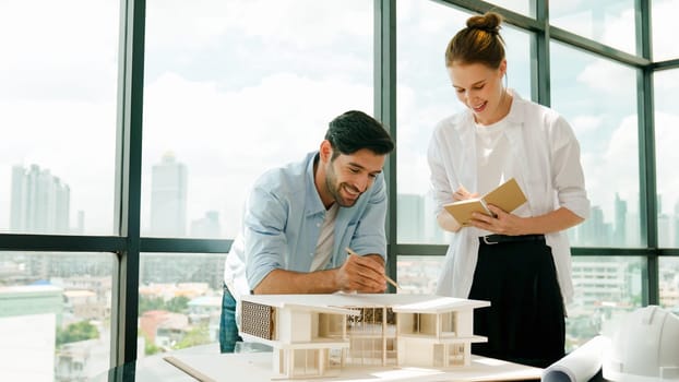 Skilled architect engineer team discussion about house model construction. Smart interior designer sharing, talking about building design while beautiful coworker taking a note. Design. Tracery