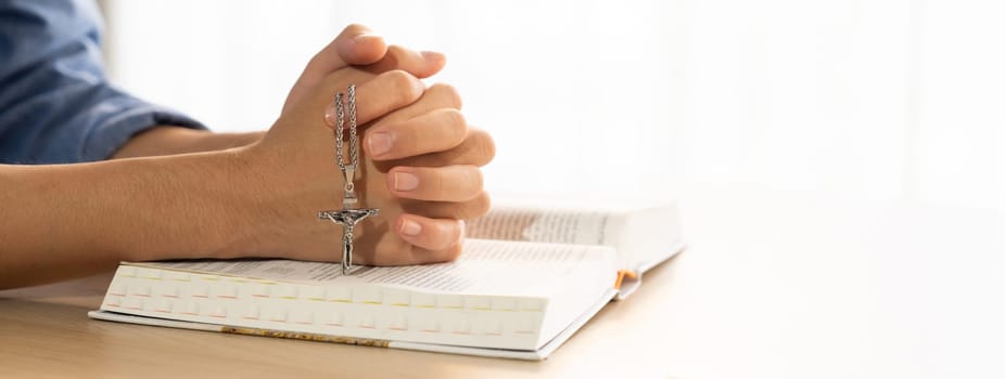 Asian male folded hand prayed on holy bible book while holding up a pendant crucifix. Spiritual, religion, faith, worship, christian and blessing of god concept. Blurring background. Burgeoning.