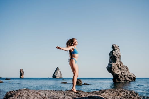 Middle aged well looking woman with black hair doing Pilates with the ring on the yoga mat near the sea on the pebble beach. Female fitness yoga concept. Healthy lifestyle, harmony and meditation.