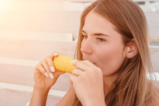 Healthy vegetarian hipster woman in summer outfit eat grilled corn and look to camera. Sexy lady on sea beach sunset or ocean sunrise. Travel, explore, active yoga and meditation lifestyle concept.