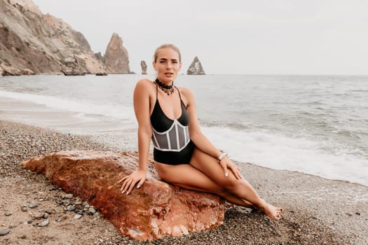 Side view a Young beautiful sensual woman in a mint long dress posing on a volcanic rock high above the sea during sunset. Girl on the nature on overcast sky background. Fashion photo