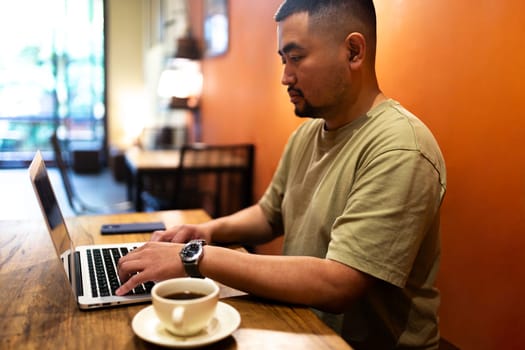 Asian man working with laptop in coffee shop. Copy space. Freelance concept.