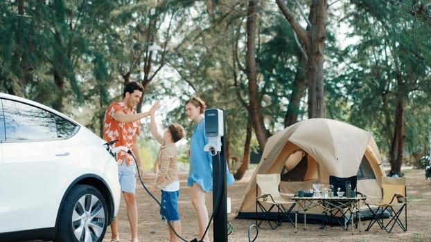 Outdoor adventure and family vacation camping in nature travel by eco friendly car for sustainable future. Lovely family recharge EV car with EV charging station in campsite. Perpetual