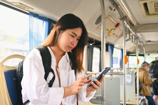 Beautiful young woman using smartphone while while riding a bus in the city.