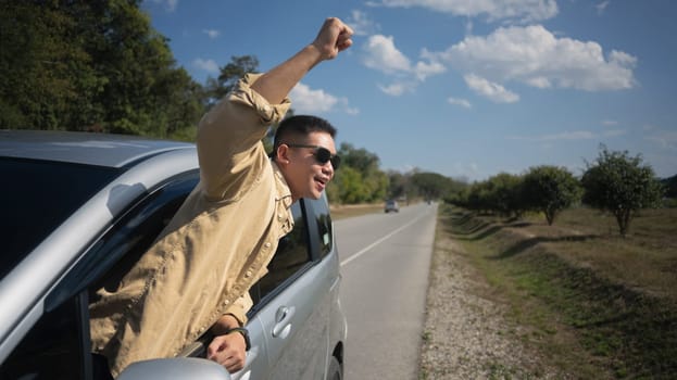 Joyful young man on the road trip travel vacation leaning out from car window. Travel and transportation concept.