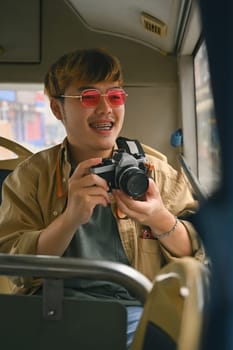 Young man tourist in pink glasses holding camera enjoying the travel on bus.