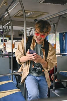 Portrait of smiling man tourist traveling by bus and using mobile phone. People and transportation concept.