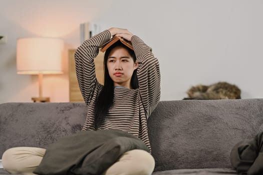 Young Asian woman put a book on her head, looking tired or bored.