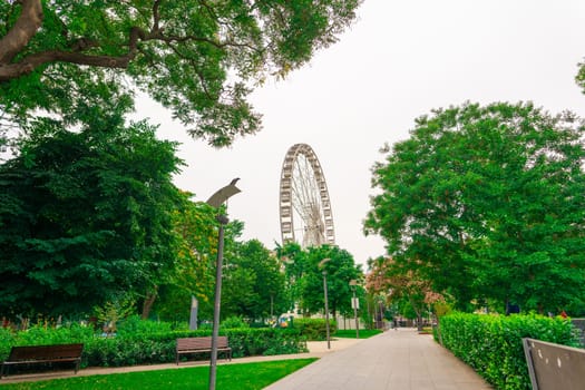 Ferris wheel featuring colourful seating pods against backdrop of sky and green flowers in city park