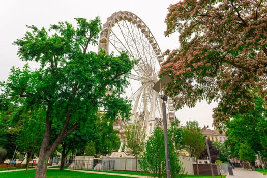 Ferris wheel featuring colourful seating pods against backdrop of sky and green flowers in city park