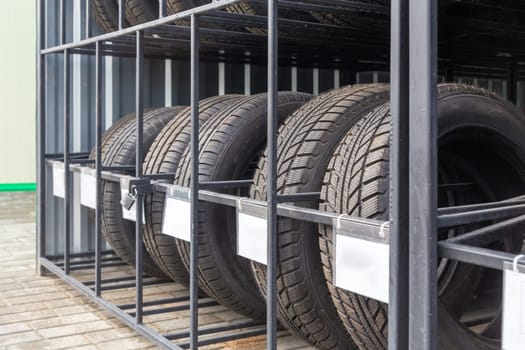 Close-up image of new car tires arranged on metal shelving in outdoors shop. Clean information plates for information placement.