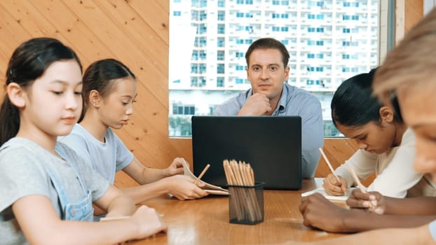 Caucasian teacher and smart boy discuss about project at classroom. Professional instructor talking about classwork while giving a paper to highschool child with diverse student listen. Edification.