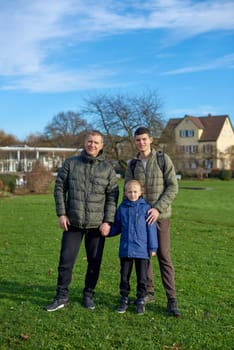 Family Harmony: Father, 40 Years Old, and Two Sons - Beautiful 8-Year-Old Boy and 17-Year-Old Young Man, Standing on the Lawn in a Park with Vintage Half-Timbered Buildings, Bietigheim-Bissingen, Germany, Autumn. Embrace the essence of family togetherness with this heartwarming image featuring a father, 40 years old, and his two sons - a beautiful 8-year-old boy and a 17-year-old young man. Standing on the lush lawn in a park with vintage half-timbered buildings in Bietigheim-Bissingen, Germany, this captures the warmth of familial bonds amidst the autumnal beauty.