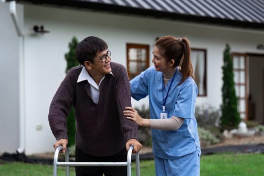 Nurse or caregiver helps elderly walk by using walker in garden.