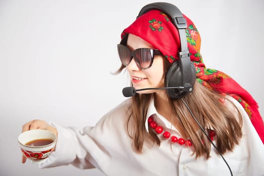 Portrait of young girl in a bright red scarf and large headphones with a microphone. A woman who is radio or television presenter with cap of tee. Funny female telecom operator. Freelancer at work