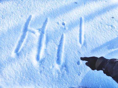 Inscription Hi, written on white background of the snow. Top view. Flat lay. New year and Christmas. Greeting morning, day, weather, sun and people