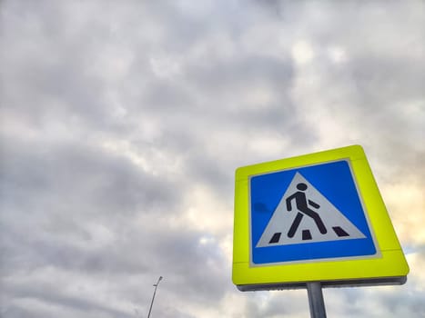 A pedestrian crossing sign on the background of a gray sky with clouds. Drawing, pictogram for pedestrians crossing the road
