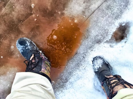 Feet of Hunter or fisherman in big warm boots on winter day on snow. Top view. Fisherman on the ice of a river, lake, reservoir on spring day with melting ice. Dangerous fishing in autumn