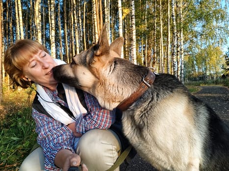 Adult girl with shepherd dog taking selfies in forest. Middle aged woman and big shepherd dog on nature. Friendship, love, communication, fun, hugs