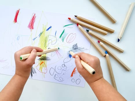 small child draws with colored pencils on paper on white table. High quality photo