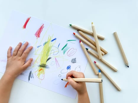 small child draws with colored pencils on paper on white table. High quality photo