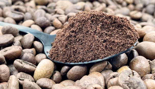 Against the background of roasted aromatic coffee beans lies a metal spoon filled with ground coffee. A drink made from roasted and ground beans from the coffee tree or coffee bush