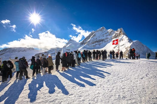 Tourists waiting in line to take a photo in front of Swiss flag on Jungfraujoch peak, Berner Oberland region of Switzerland
