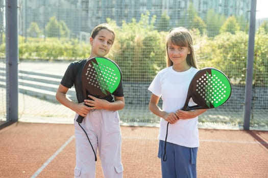 Teenage girls with racquets and balls standing in padel court, looking at camera and smiling. High quality photo